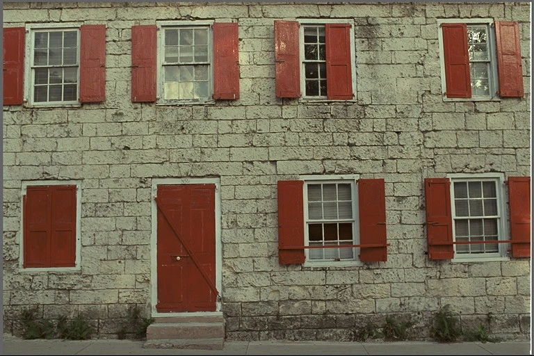 Reference photograph of a stone house with red window shutters.